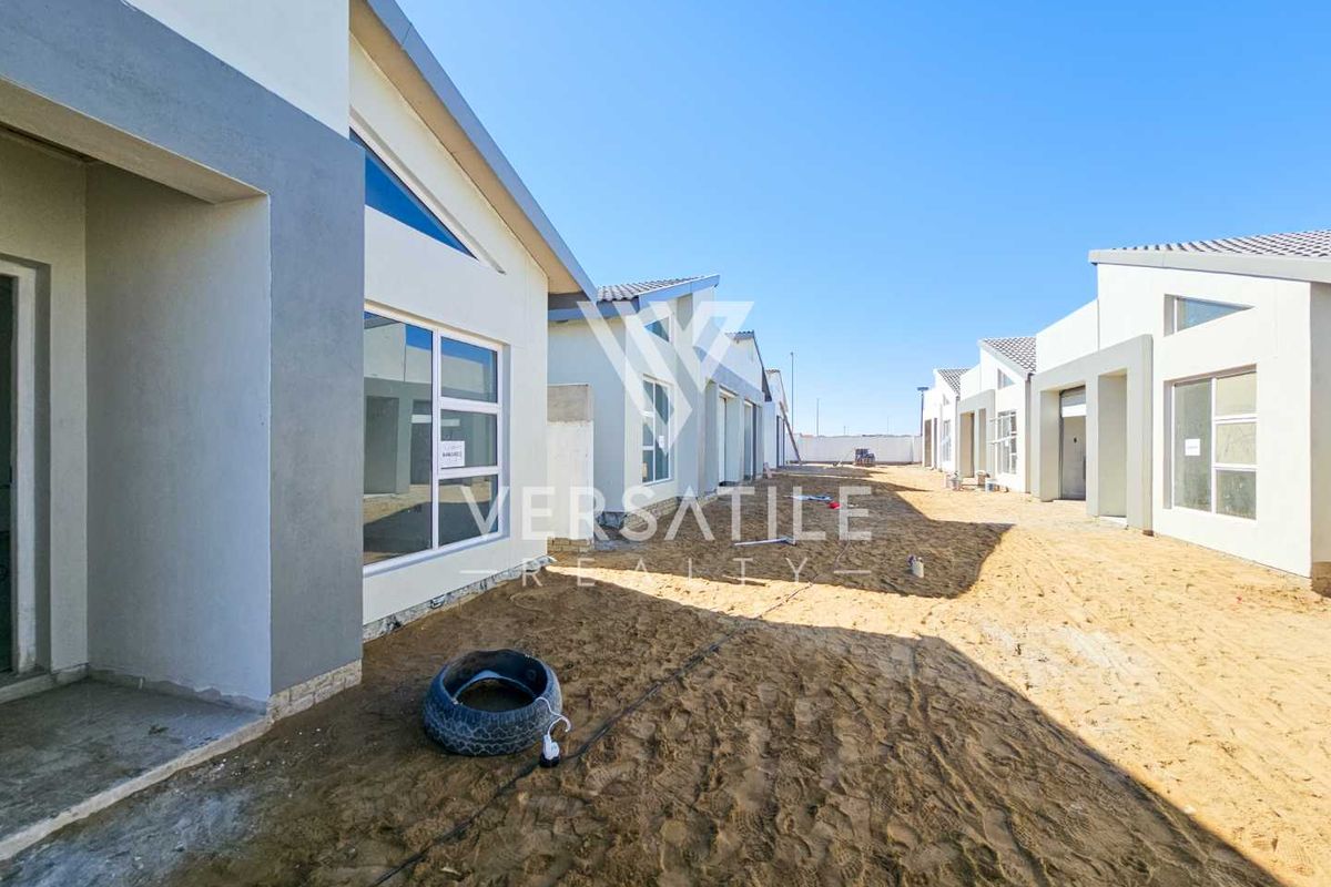Exterior view of a townhouse development showing unfinished ground and modern plastered facades with aluminium window frames.