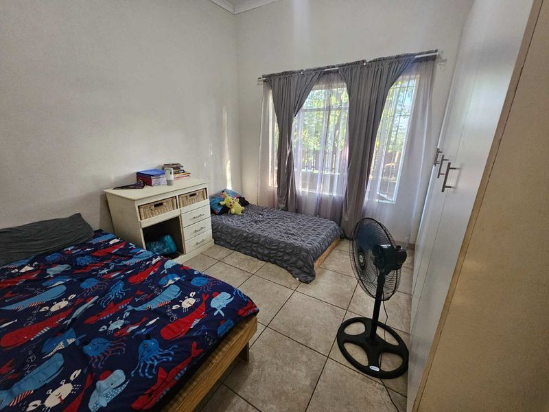 A functional bedroom featuring tiled flooring, a built-in wardrobe, and large windows with curtain rails, providing ample natural light.