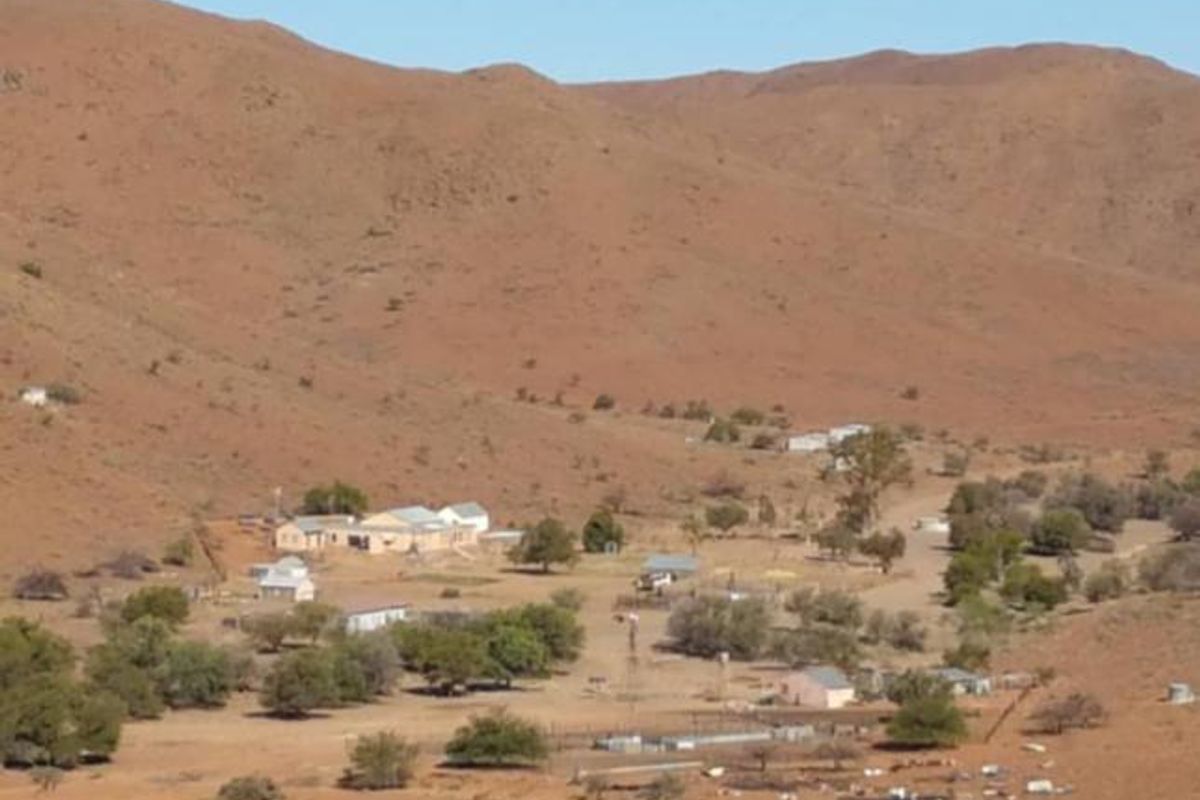 An elevated aerial view of a rural farm property set within a vast, arid mountainous landscape.