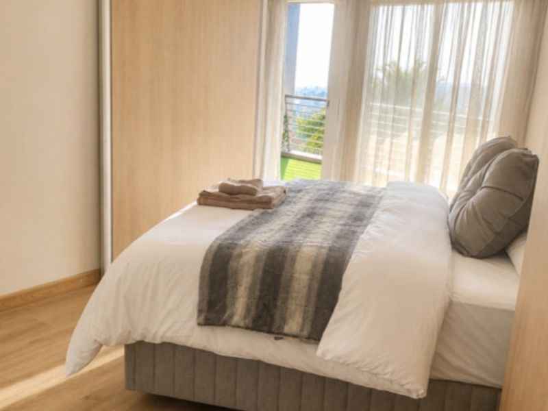 A bright bedroom featuring modern laminate flooring, built-in sliding door wardrobes, and direct access to a private balcony through sliding glass doors.