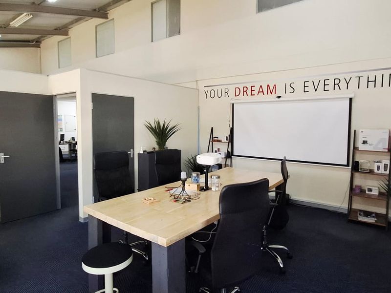 A functional office space featuring high ceilings with exposed structural elements, clerestory windows for natural light, and a wall-mounted projector screen.