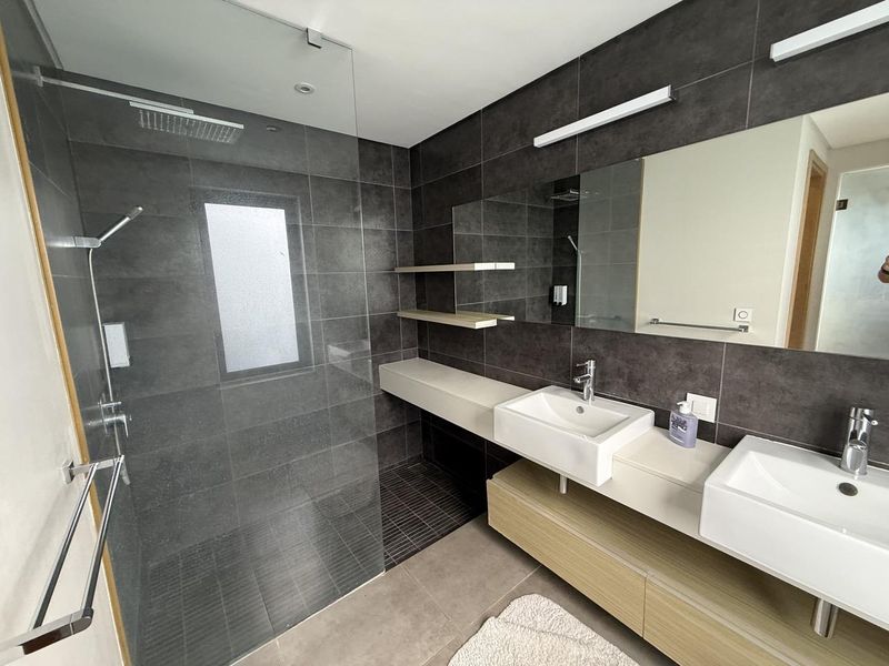 Modern bathroom featuring a double vanity with floating cabinetry, a spacious walk-in shower with a rain shower head, and contemporary dark tile finishes.