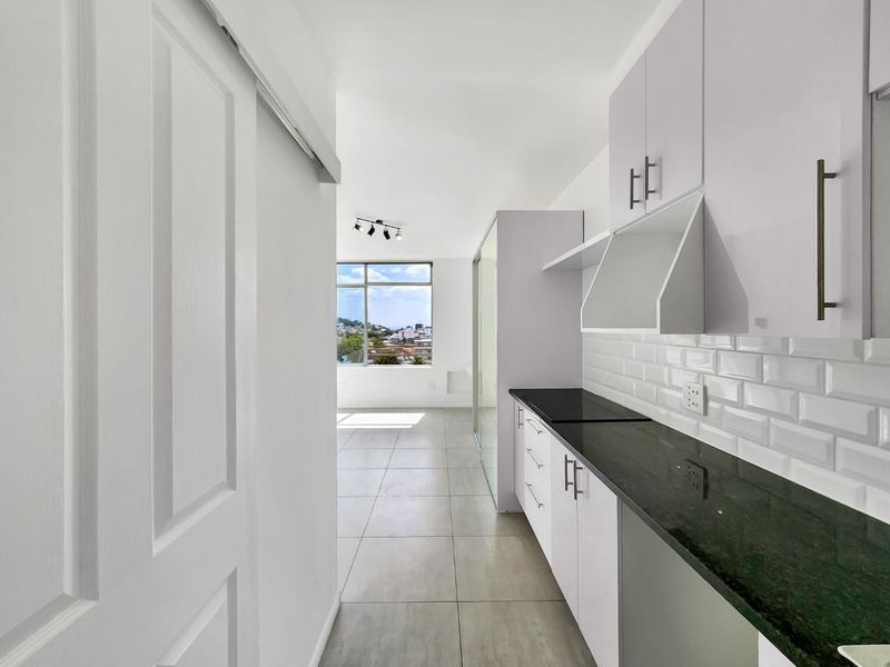 Modern kitchen featuring white cabinetry, black granite countertops, and a classic subway tile backsplash, leading into a bright, open-plan living area with city views.
