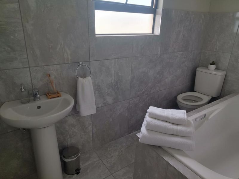 A modern bathroom featuring grey tiled walls and flooring, a pedestal basin, a toilet, and a bathtub.