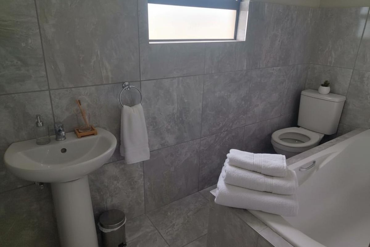 A modern bathroom featuring grey tiled walls and flooring, a pedestal basin, a toilet, and a bathtub.