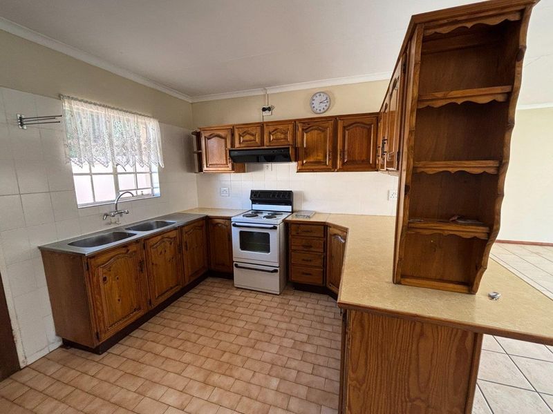 A functional kitchen featuring traditional wooden cabinetry, laminate countertops, a double sink, and a freestanding stove with an extractor fan.