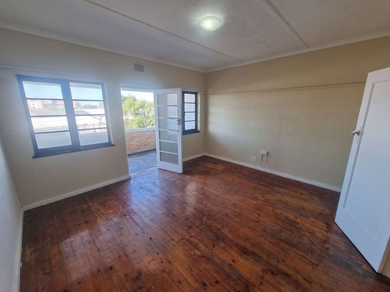 An empty bedroom featuring original hardwood flooring, large windows, and direct access to an outdoor balcony area.