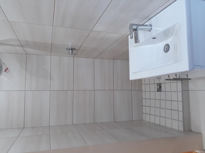 A clean, modern bathroom featuring white wall tiles, a wall-mounted basin with a chrome mixer tap, and a shower fixture.
