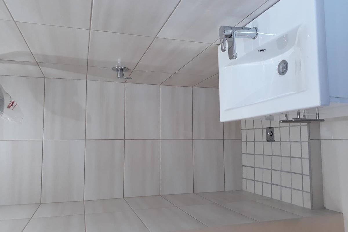 A clean, modern bathroom featuring white wall tiles, a wall-mounted basin with a chrome mixer tap, and a shower fixture.