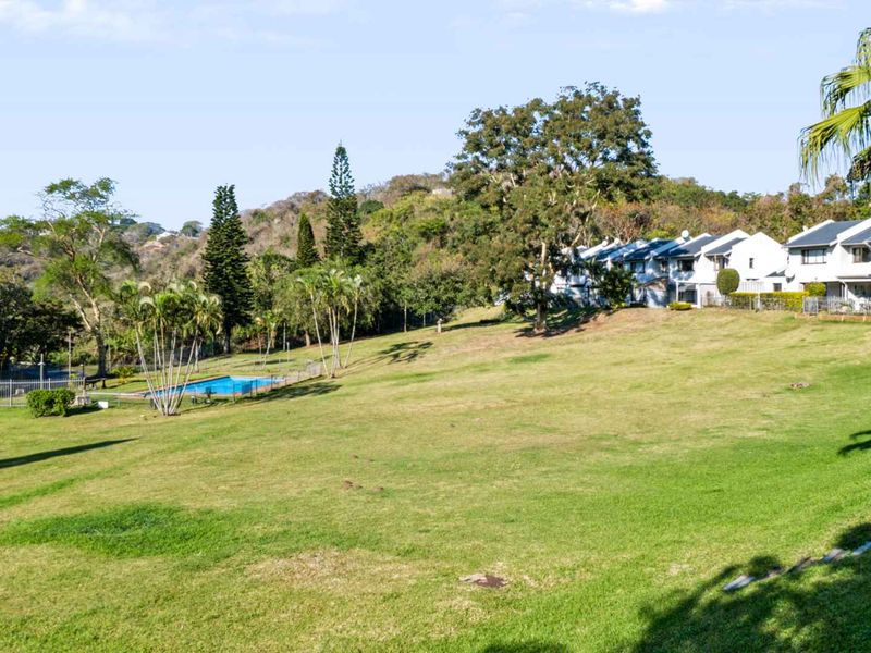 A wide-angle view of the townhouse complex rear grounds, featuring a communal swimming pool, expansive lawn, and established trees.