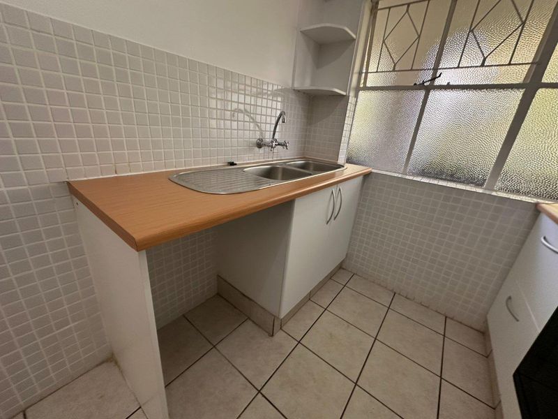 A functional kitchen area featuring a stainless steel sink, laminate countertop, tiled backsplash, and built-in cabinetry with tiled flooring.