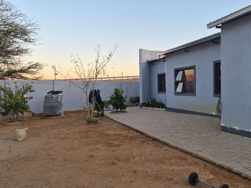 Rear exterior view of the house featuring a paved patio area, perimeter wall, and aluminium window frames.