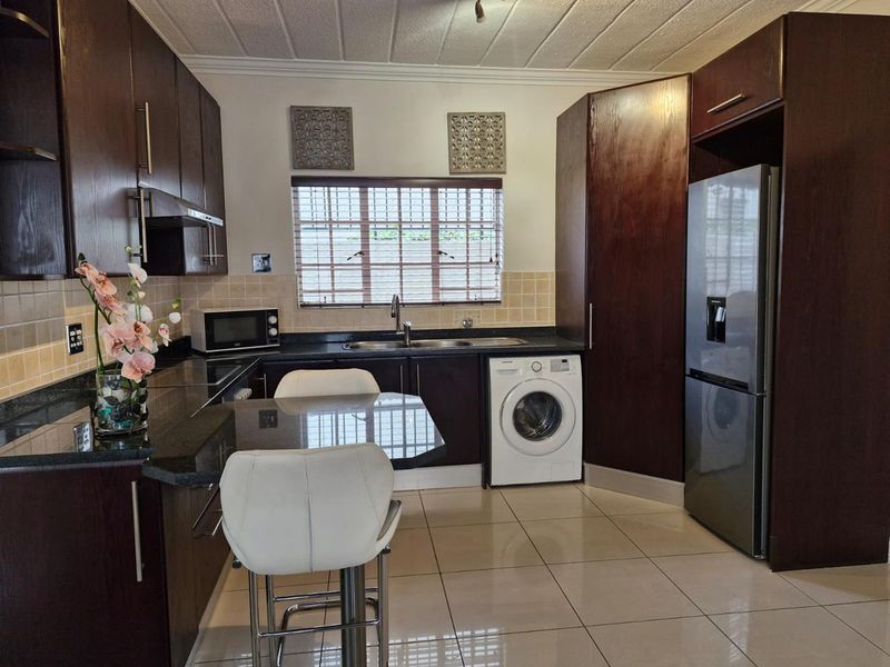 A well-maintained kitchen featuring dark wood cabinetry, granite countertops, tiled backsplash, and integrated appliance spaces with ceramic floor tiles.