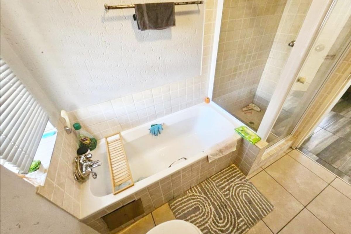 A functional bathroom featuring a built-in bathtub with tiled surround and a separate glass-enclosed shower area with ceramic floor tiling.
