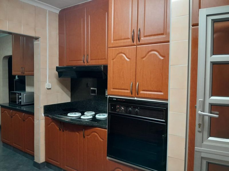 A functional kitchen featuring traditional wood-finish cabinetry, granite countertops, a built-in oven, and an electric hob with an extractor fan.