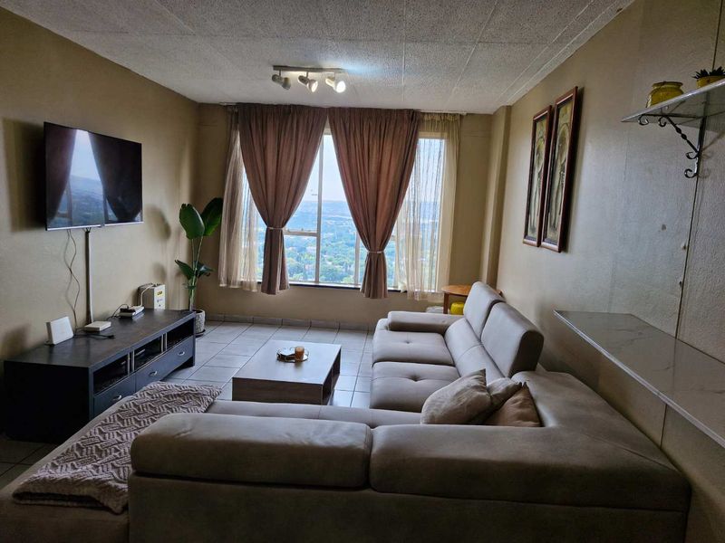 A comfortable living room featuring tiled flooring, large windows with natural light, and a view of the surrounding area.