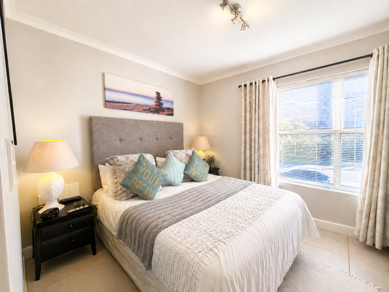 A well-maintained bedroom featuring tiled flooring, neutral wall finishes, and a large window with fitted blinds and curtains.