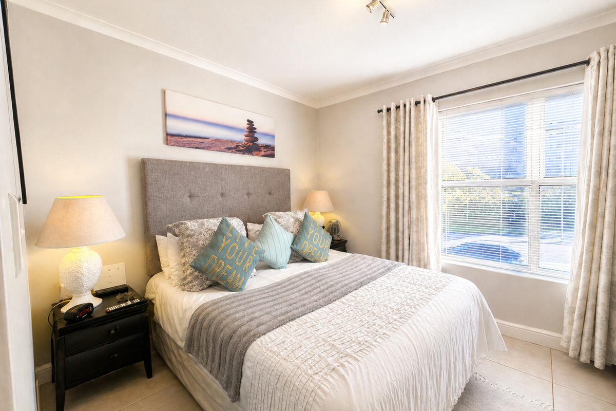 A well-maintained bedroom featuring tiled flooring, neutral wall finishes, and a large window with fitted blinds and curtains.