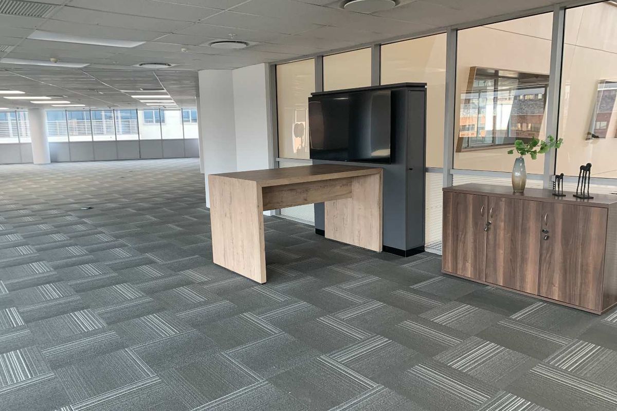 Spacious open-plan office area featuring carpet tiles, suspended ceilings with recessed lighting, and large windows providing ample natural light.