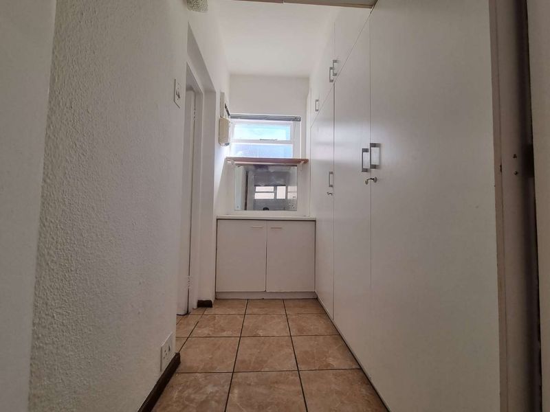 A functional scullery or utility area featuring built-in white cabinetry, tiled flooring, and a window providing natural light.