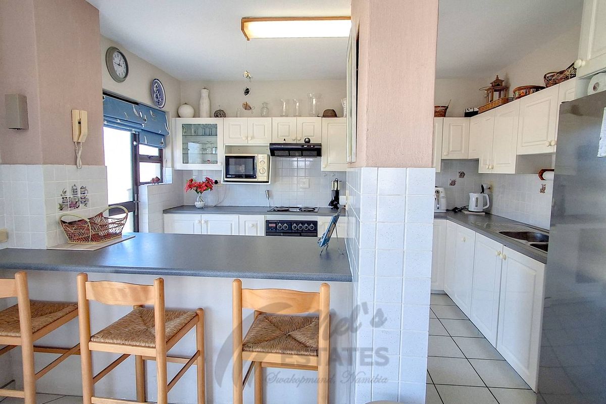 Functional kitchen featuring white cabinetry, tiled backsplash, built-in oven and hob, and a convenient breakfast bar for casual dining.