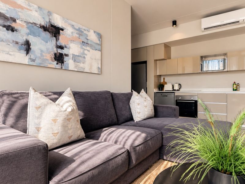 Modern open-plan living area featuring a sleek kitchen with integrated appliances, neutral cabinetry, and a wall-mounted air conditioning unit.