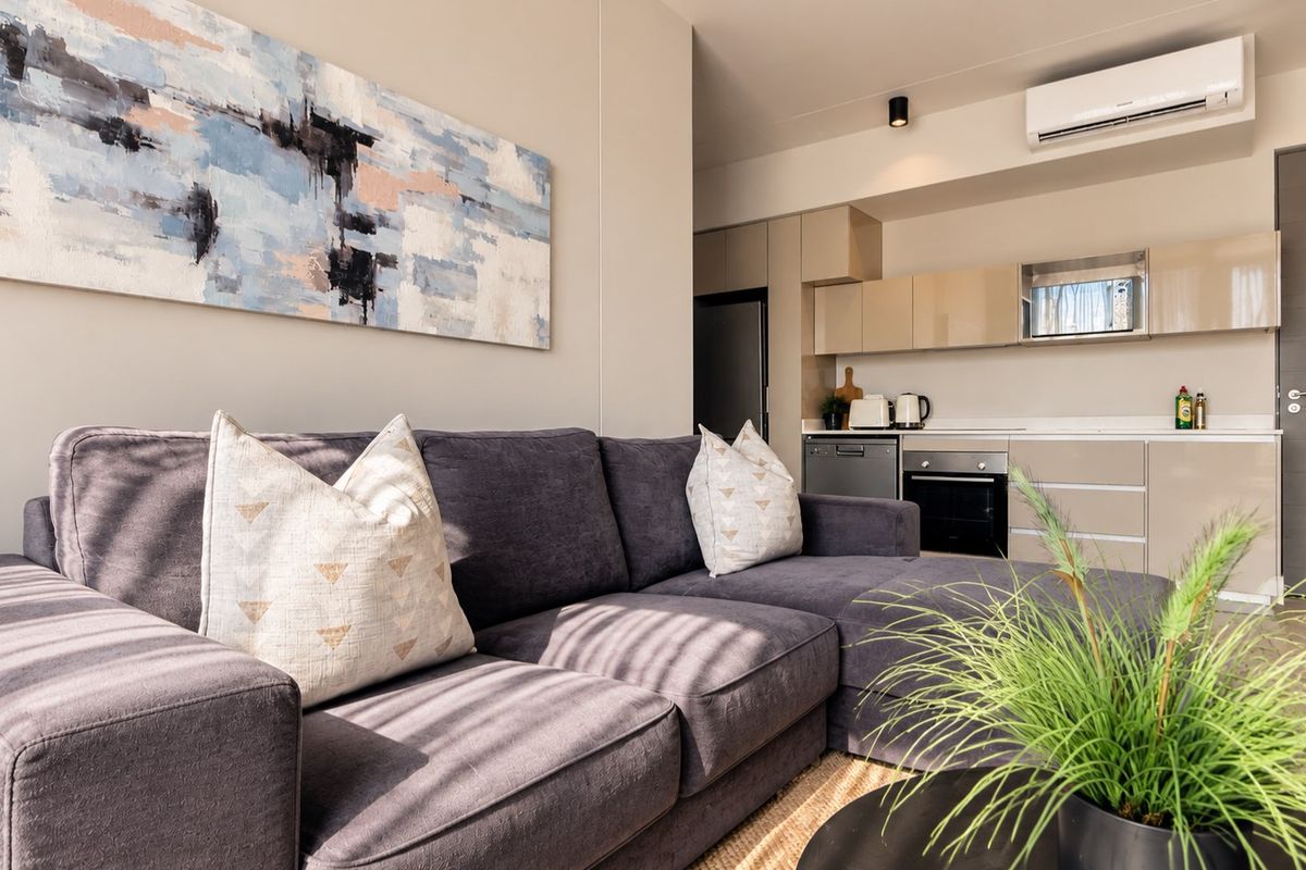 Modern open-plan living area featuring a sleek kitchen with integrated appliances, neutral cabinetry, and a wall-mounted air conditioning unit.