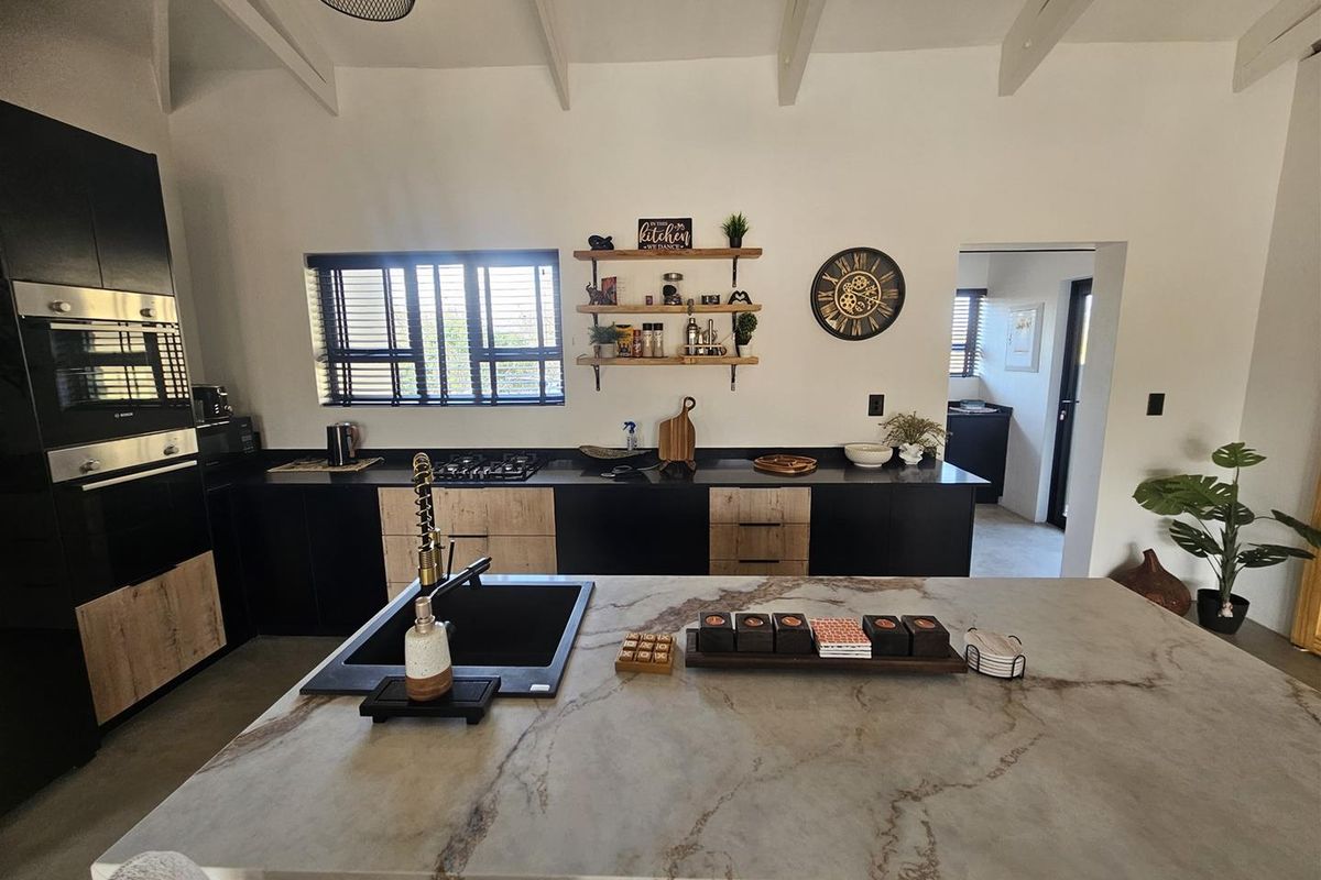 Modern kitchen featuring a large stone-topped island, built-in oven, gas hob, and sleek two-tone cabinetry with exposed ceiling beams.