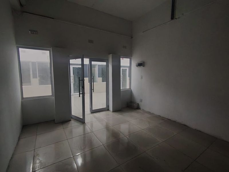 An empty, open-plan interior space featuring tiled flooring, aluminium-framed glass doors, and large windows, providing a blank canvas for potential office or living use.