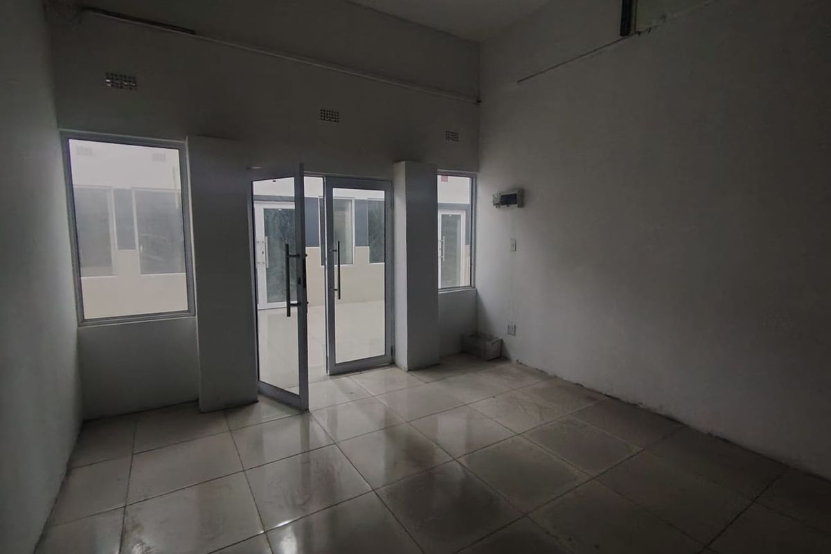 An empty, open-plan interior space featuring tiled flooring, aluminium-framed glass doors, and large windows, providing a blank canvas for potential office or living use.