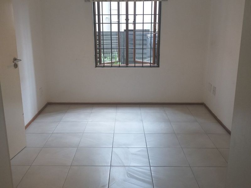 A clean, empty bedroom featuring neutral tiled flooring, white walls, and a window fitted with security bars.