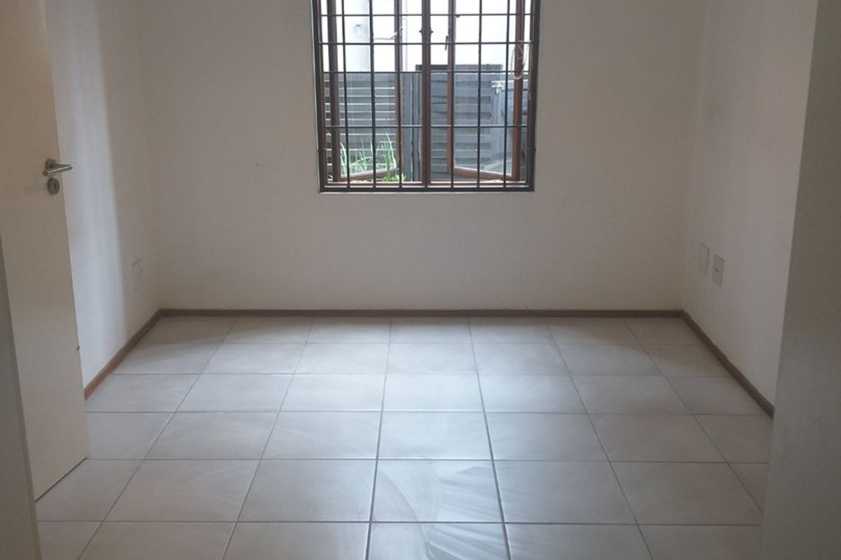 A clean, empty bedroom featuring neutral tiled flooring, white walls, and a window fitted with security bars.