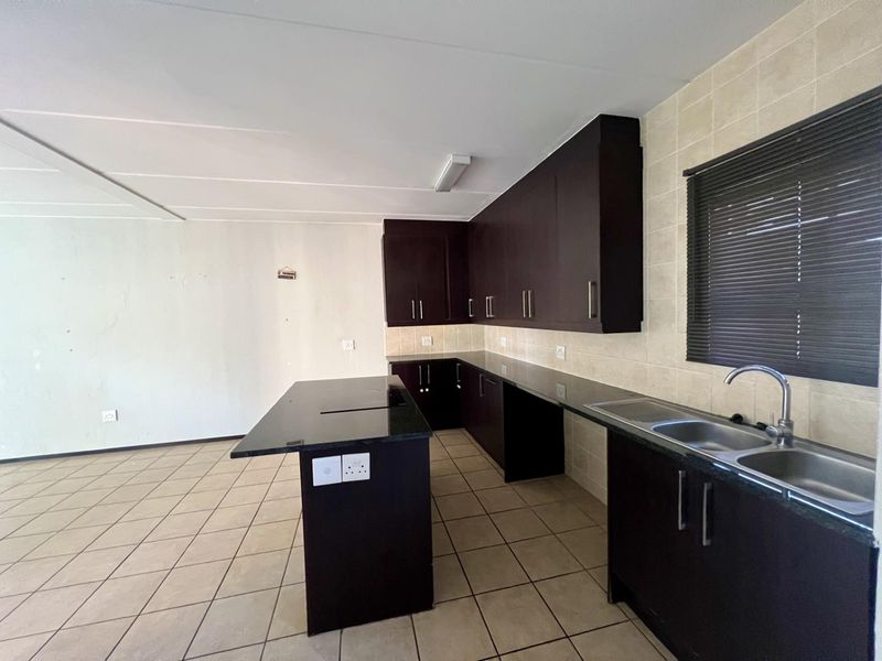 An empty kitchen featuring dark wood cabinetry, granite countertops, a central island, and a double basin sink with tiled backsplash.