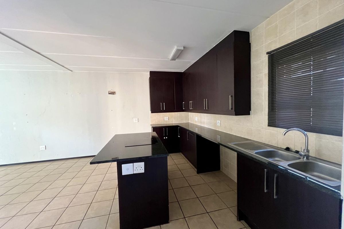 An empty kitchen featuring dark wood cabinetry, granite countertops, a central island, and a double basin sink with tiled backsplash.