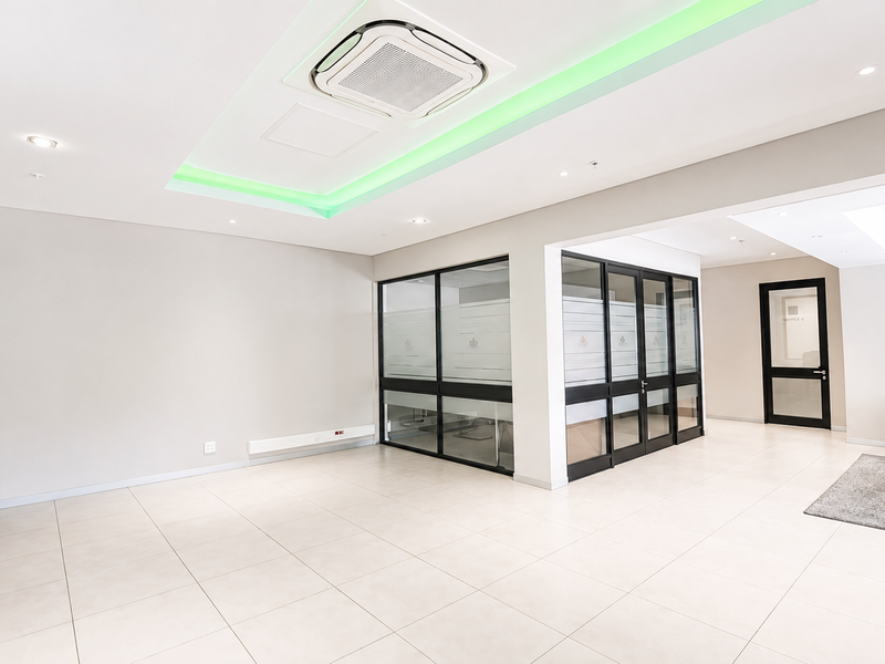Modern open-plan office space featuring tiled flooring, glass partitions, and integrated ceiling lighting with ducted air conditioning.