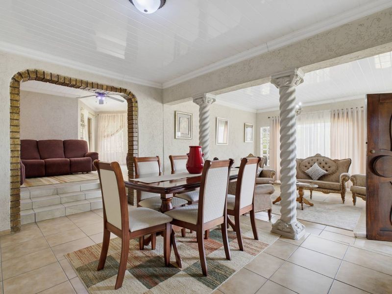 Spacious open-plan living and dining area featuring a raised platform, decorative brick archway, and classic architectural columns.