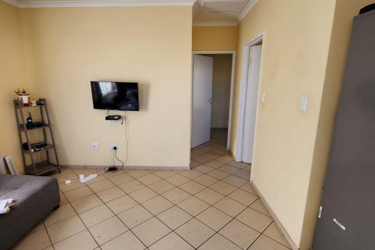 A living area featuring tiled flooring and coved ceilings, providing a functional space with access to adjacent rooms.