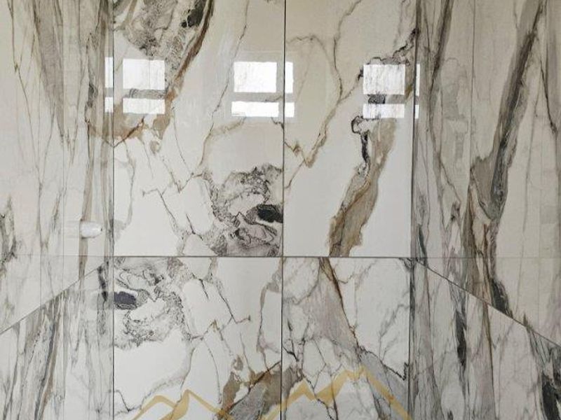 A modern shower enclosure featuring high-end marble-look wall tiling, hexagonal floor tiles, and a sleek linear drain.