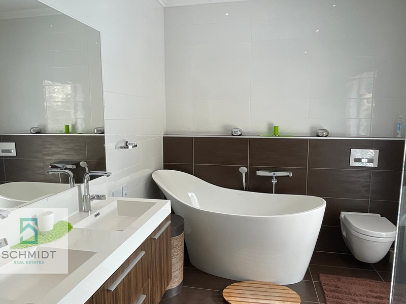 Modern bathroom featuring a sleek freestanding bathtub, wall-hung toilet, and a contemporary double vanity with a large mirror.