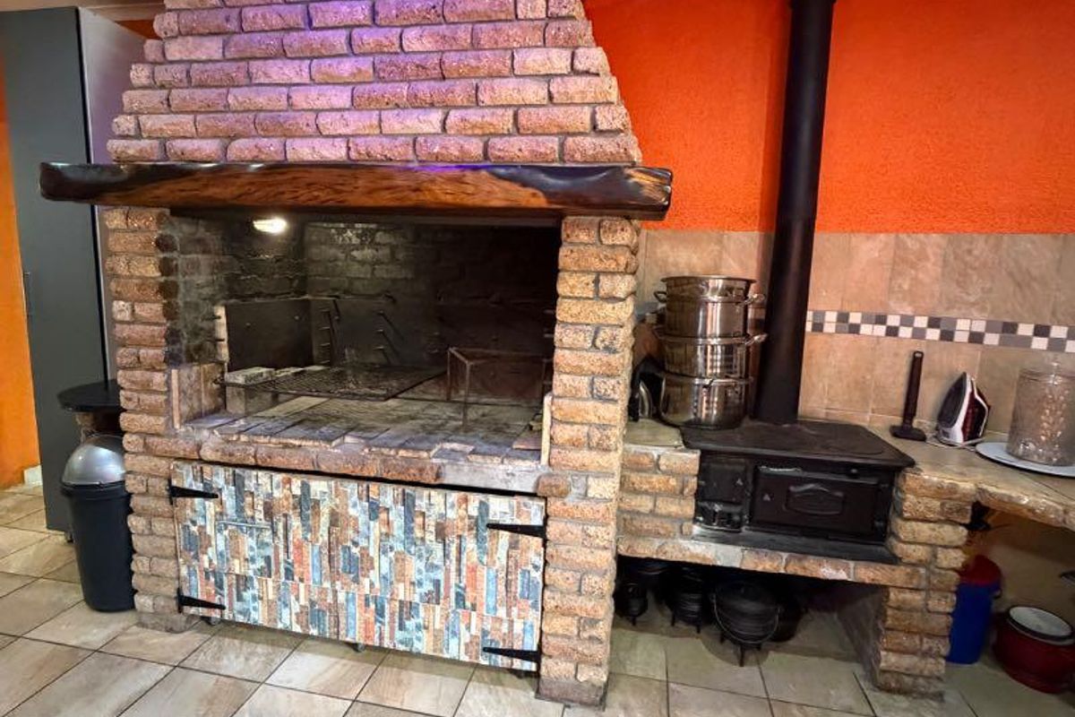 Indoor entertainment area featuring a large built-in brick braai, wood-burning stove, and tiled flooring.