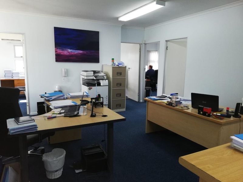 A functional office space featuring blue carpet flooring, fluorescent lighting, and multiple internal doorways providing access to adjacent rooms.