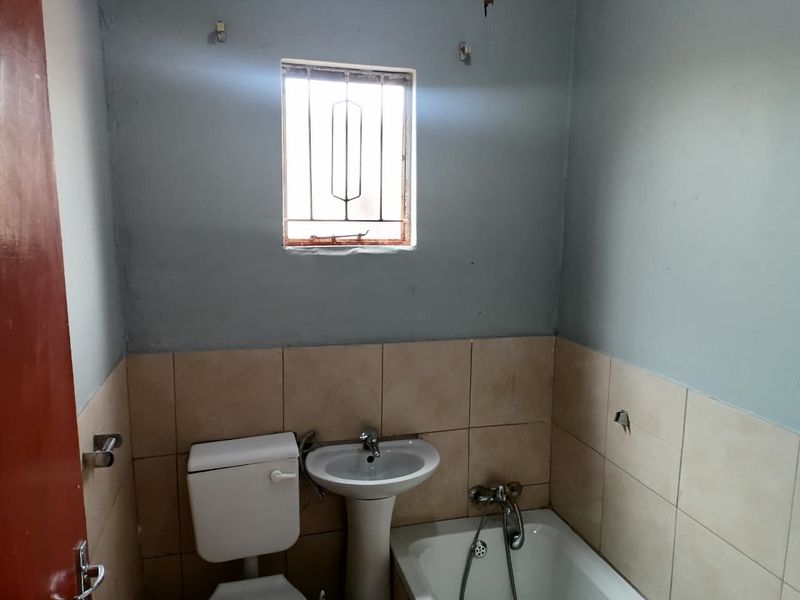 A functional bathroom featuring a pedestal basin, toilet, and bathtub with tiled splashbacks, requiring cosmetic updates to improve its overall condition.