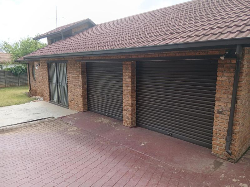Exterior view of a brick-faced house featuring a double garage with roller doors and an adjacent sliding door entrance with security gate.