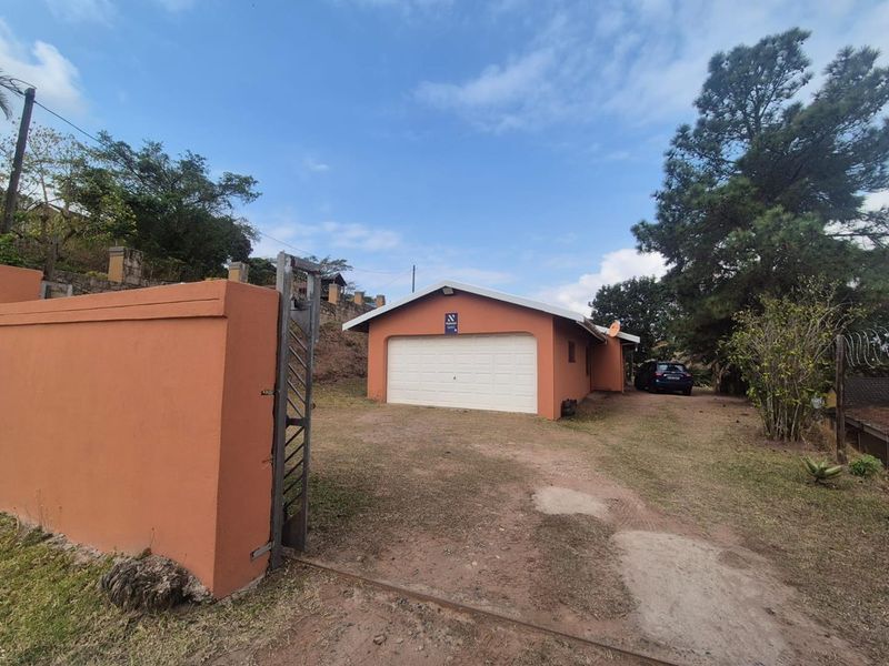Front view of a detached garage with a white sectional door, enclosed by a perimeter wall and metal gate on an unpaved lot.