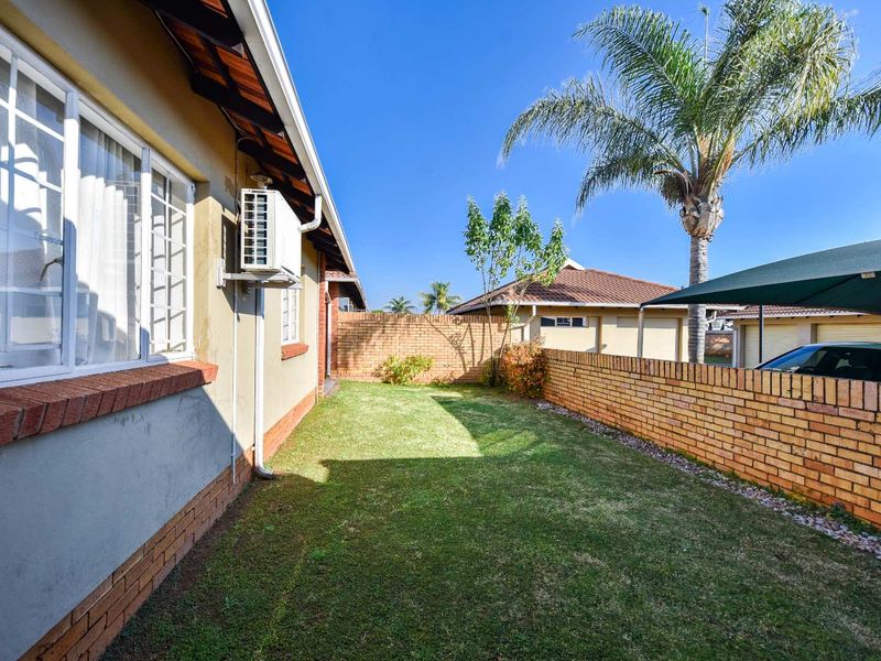 A well-maintained rear garden area featuring a brick boundary wall, lawn, and an exterior wall-mounted air conditioning unit.