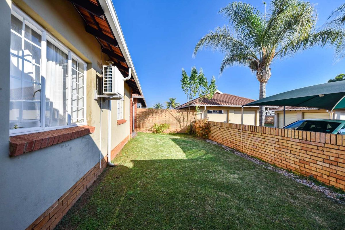 A well-maintained rear garden area featuring a brick boundary wall, lawn, and an exterior wall-mounted air conditioning unit.