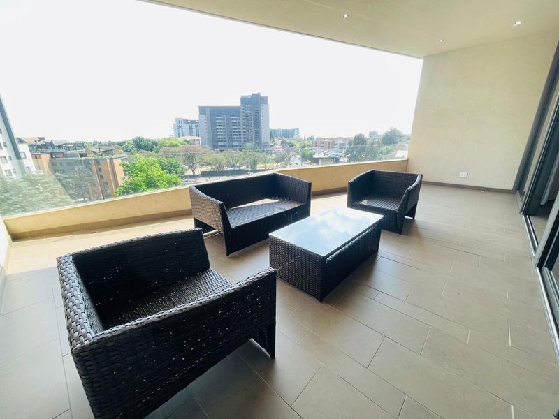 Spacious covered balcony featuring tiled flooring, recessed lighting, and a modern glass balustrade offering expansive urban views.