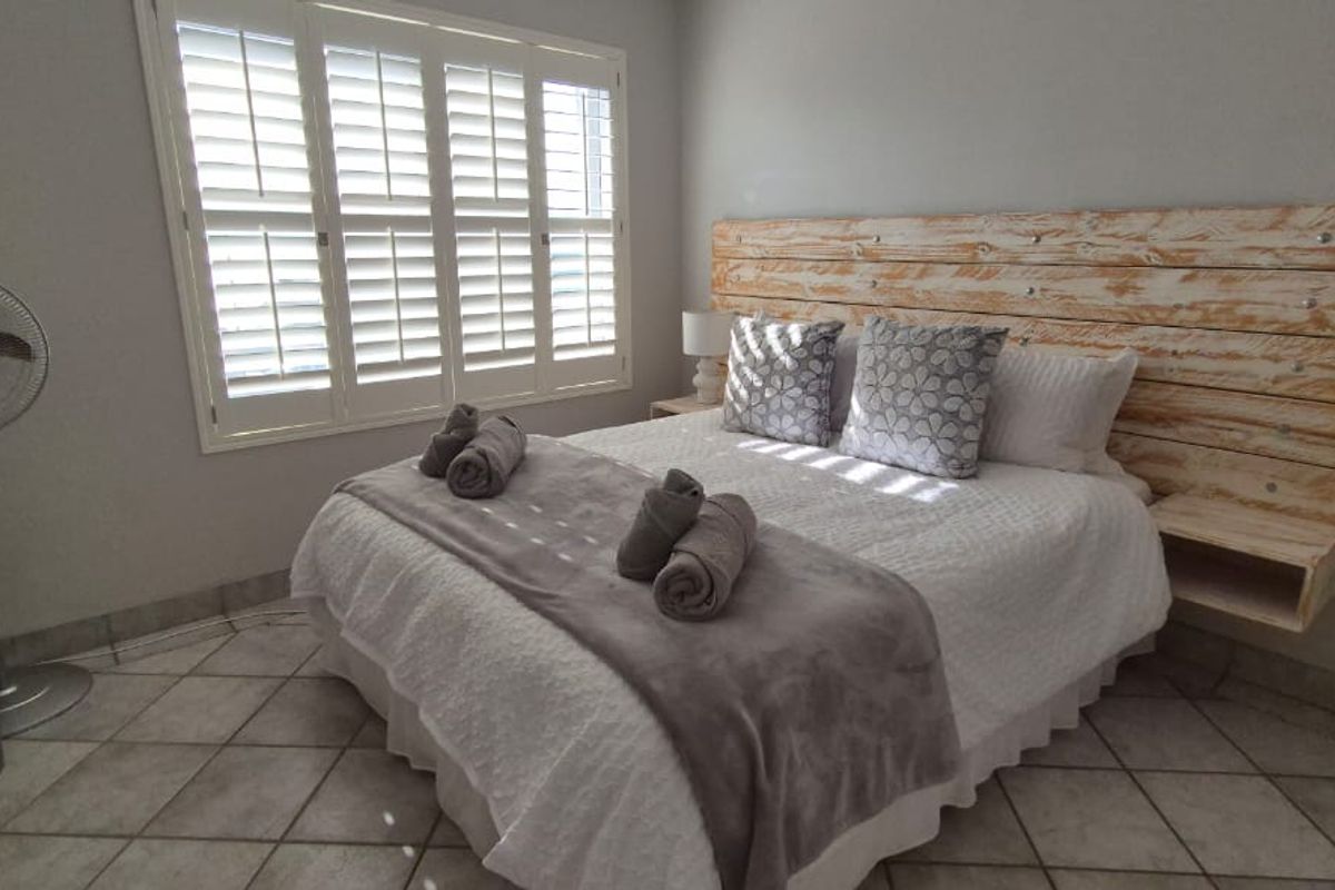 A bedroom featuring tiled flooring and white plantation shutters, providing a clean and functional space.