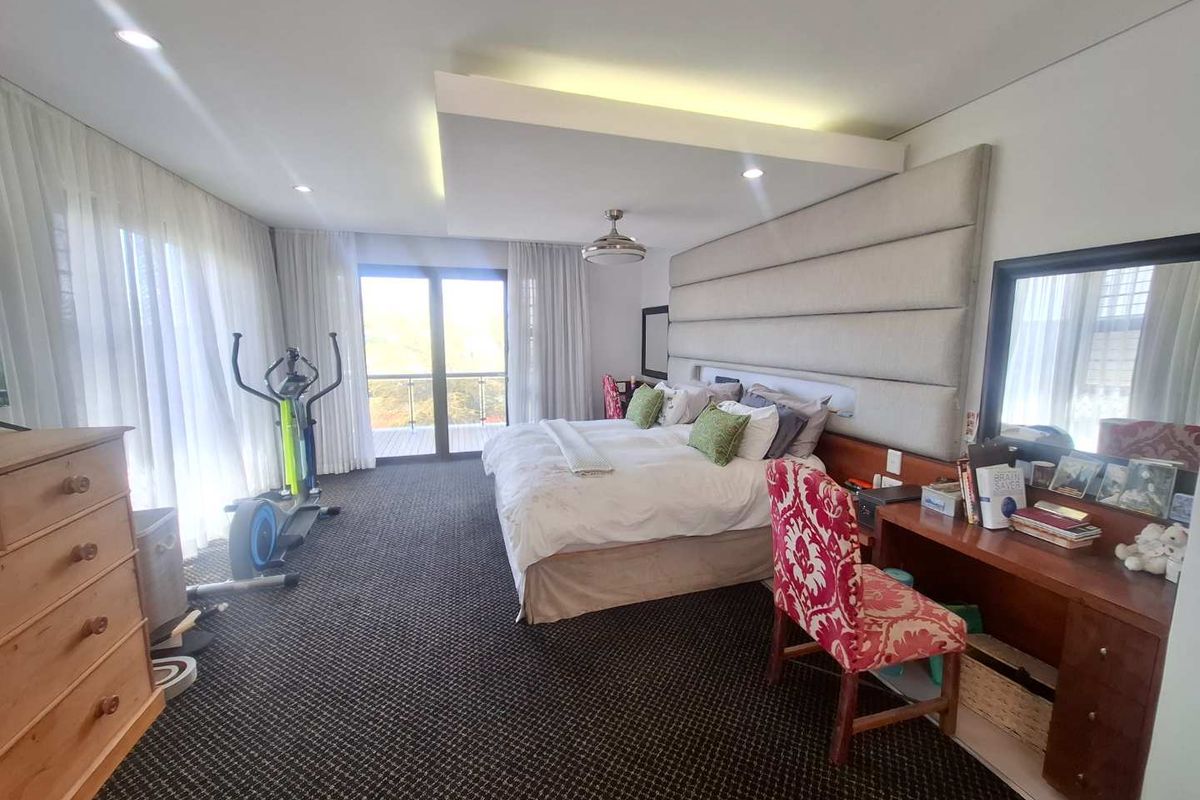 Spacious bedroom featuring a large upholstered headboard wall, recessed ceiling lighting, a built-in vanity, and sliding glass doors leading to a balcony.