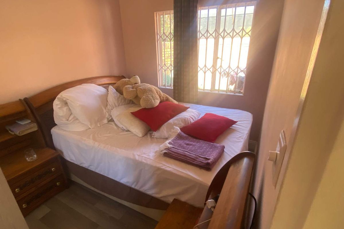A compact bedroom featuring laminate flooring and a window fitted with security bars, providing natural light.